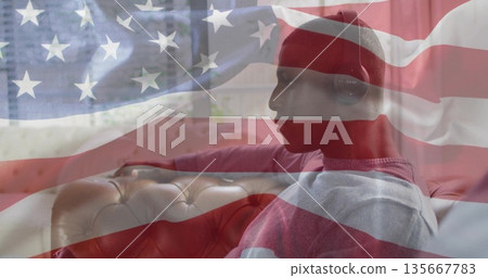 Sitting man wearing beanie and headset listening on couch near window with flag overlay, copy space Sitting man wearing beanie and headset listening on couch near window with flag overlay, copy space 135667783