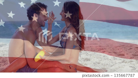 bikini clad woman applying sunscreen onto man with sponge on shoreline, with US flag graphic bikini clad woman applying sunscreen onto man with sponge on shoreline, with US flag graphic 135667787