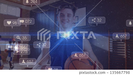 Smiling man wearing blue jersey holding orange basketball on gym court, with digital notifications 135667798