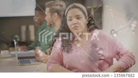 Leaning woman wearing pink sweater analyzing network graphic at office table, with laptops, mug Leaning woman wearing pink sweater analyzing network graphic at office table, with laptops, mug 135667882