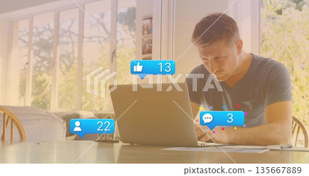 Mature man typing on silver laptop in dining workspace, with papers pen plant and social icons 135667889