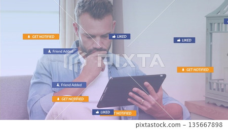 Mid-adult man holding tablet on couch at home, with floating notification icons and birdcage Mid-adult man holding tablet on couch at home, with floating notification icons and birdcage 135667898
