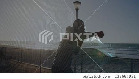 Throwing forward punch athlete wearing hoodie and boxing gloves on seaside promenade, with railing Throwing forward punch athlete wearing hoodie and boxing gloves on seaside promenade, with railing 135667951