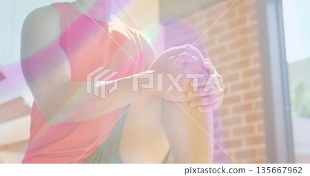 Performing fitness man holding knee-to-chest stretch in brick-walled workout area, under sunlight 135667962