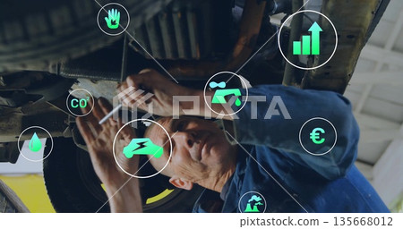 Working mechanic using wrench under vehicle lift in brightly lit garage with digital icons 135668012