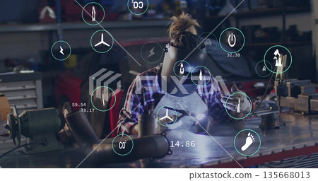 Welding female welder wearing helmet leaning on workbench, casting torch arc with digital overlays 135668013