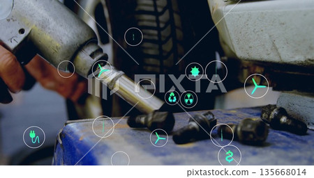 Gloved hand tightening lug nut on tire with impact wrench in workshop, energy icons, copy space 135668014