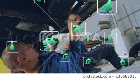 Wrenching mechanic wearing blue coverall addressing car undercarriage in workshop, with green icons Wrenching mechanic wearing blue coverall addressing car undercarriage in workshop, with green icons 135668015