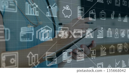 Holding digital tablet clinician wearing blue top with stethoscope in clinic, with financial icons 135668042