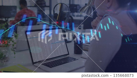Analyzing spreadsheet woman wearing dark top working at open-plan office, with laptop, stock charts 135668073