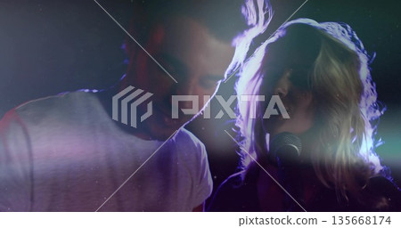 Musical duo performing on dark stage, with microphone, colored lights and audio cables 135668174