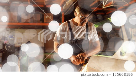 Grinding craftsman wearing overalls at workshop bench with angle grinder, sending sparks Grinding craftsman wearing overalls at workshop bench with angle grinder, sending sparks 135668196