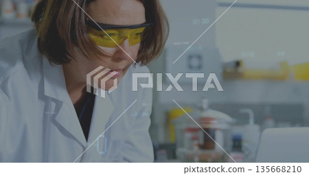 Female scientist wearing lab coat analyzing data at bench with glassware and laptop, copy space Female scientist wearing lab coat analyzing data at bench with glassware and laptop, copy space 135668210
