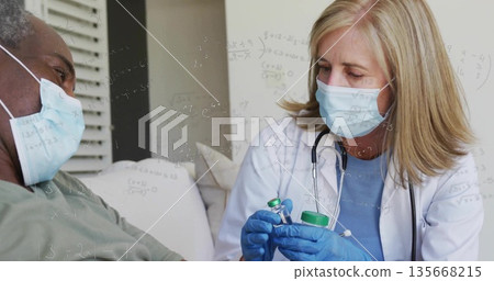 Drawing vaccine from green cap vial by masked gloved provider on couch at home, with syringe 135668215