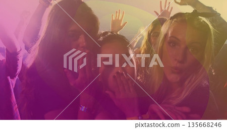 Blowing kisses three friends dancing on nightclub dance floor, with stage light haze and wristbands 135668246