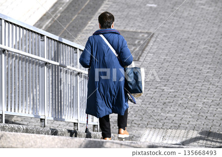 日本橫濱的城市景觀，陡峭的樓梯…老化社會。一位拄著拐杖的老婦人（擺出姿勢）。她下樓梯似乎很吃力。樓梯陡峭，令人望而生畏… 135668493