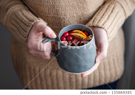 A woman holds a mug of non-alcoholic mulled wine or a spicy hot drink with orange A woman holds a mug of non-alcoholic mulled wine or a spicy hot drink with orange 135669385