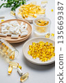 Yellow and white vitamins capsules scattered in a different plates on a light background close up. 135669387