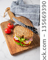 Sandwich with ham, cheese, lettuce, vegetables and seeded bread on a wooden board 135669390