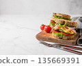Two sandwiches with ham, cheese, lettuce, vegetables and seeded bread on a wooden board 135669391
