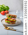 Sandwich or toast with ham, cheese, lettuce and vegetables on a plate on a gray tile 135669392