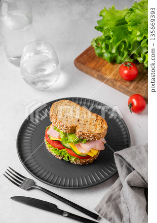 Sandwich with ham, cheese, lettuce and vegetable on a black plate on a concrete table Sandwich with ham, cheese, lettuce and vegetable on a black plate on a concrete table 135669393