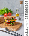 Sandwich with ham, cheese, lettuce and vegetable on a wooden board on a light background 135669396