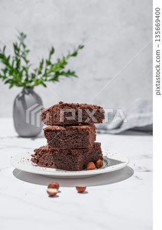 Chocolate brownie on a plate on a marble background with nuts branch and morning shadow. Chocolate brownie on a plate on a marble background with nuts branch and morning shadow. 135669400