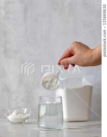 white protein powder is poured into glass with water white protein powder is poured into glass with water 135669638