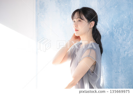 Profile of a woman posing in the sunlight against a light blue background. Image of upper body e-line 135669975