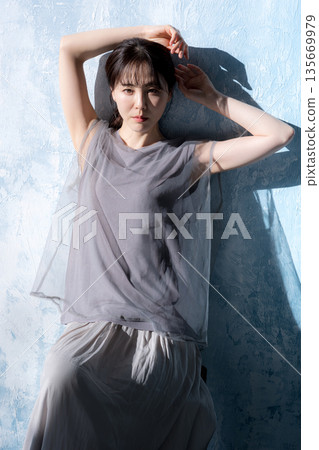 A woman posing in the sunlight against a light blue background, looking at the camera A woman posing in the sunlight against a light blue background, looking at the camera 135669979