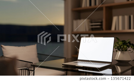 White screen laptop and potted plant on glass table and metal chair aside bookshelf and window wall. 135671422