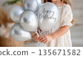 Young caucasian girl holding silver birthday balloons in white dress 135671582