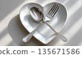Heart-shaped white plate with fork and spoon on light background 135671586