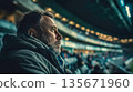 Thoughtful sports fan watching game at stadium at night, emotional portrait, crowd light, private moment in arena 135671960