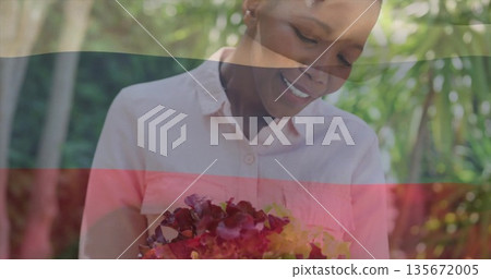 Mid adult gardener wearing pink shirt holding vibrant lettuce planter in backyard with wooden fence 135672005