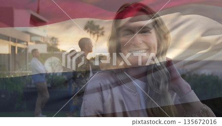 Smiling adult woman wearing bomber jacket adjusting hair on terrace at sunset, with palm trees Smiling adult woman wearing bomber jacket adjusting hair on terrace at sunset, with palm trees 135672016