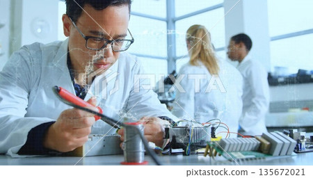 Soldering technician in lab coat using soldering iron leaning over lab bench with circuit boards 135672021