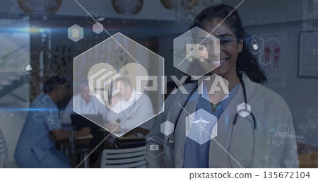 Smiling physician wearing white coat and stethoscope standing in clinic room, with medical icons 135672104