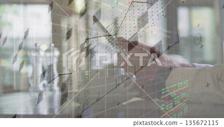 Arm wearing shirt tapping touchscreen device with stylus at desk by window, with mug, market charts 135672115