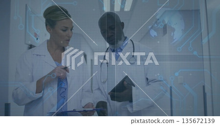 Holding clipboard and tablet, two lab coat doctors standing in hospital corridor, with blue overlay 135672139