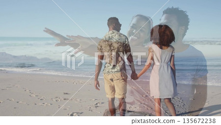 Walking couple holding hands along sandy shoreline, with footprints and gentle ocean waves 135672238
