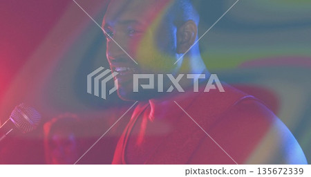 Performing musician in sweater strumming guitar at mic stand on club stage, with colorful lighting Performing musician in sweater strumming guitar at mic stand on club stage, with colorful lighting 135672339
