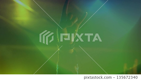 Displaying right hand forming rock horns under green concert lighting, with wristbands, lens flares Displaying right hand forming rock horns under green concert lighting, with wristbands, lens flares 135672340