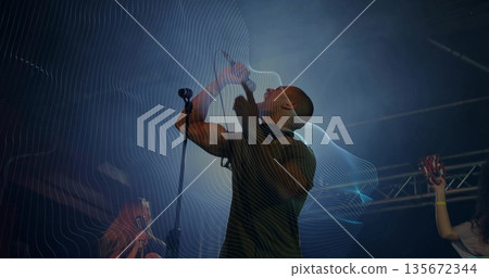 Singing lead vocalist gripping microphone on dark concert stage, with tambourine, spotlights, haze 135672344
