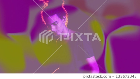 Standing male performer wearing t-shirt and cord necklace on stage, with magenta green projections 135672345