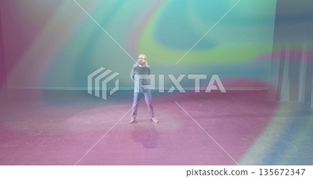 Standing adult man observing swirling multicolored spotlight patterns on theater stage 135672347
