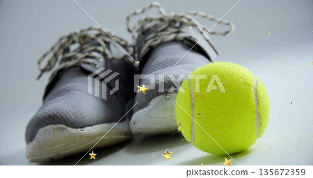 Showcasing gray athletic sneakers resting on studio surface with tennis ball and golden stars Showcasing gray athletic sneakers resting on studio surface with tennis ball and golden stars 135672359