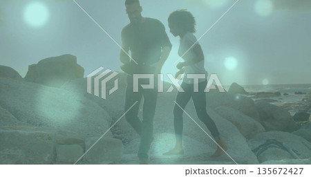 Walking friends negotiating large smooth boulders on rocky coastal shoreline, with wide-brimmed hat Walking friends negotiating large smooth boulders on rocky coastal shoreline, with wide-brimmed hat 135672427