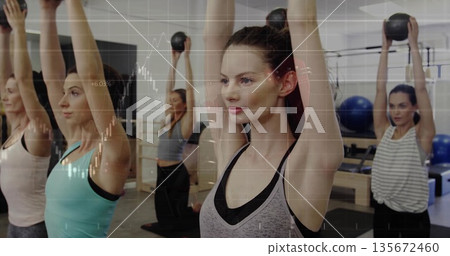 Lifting kettlebells overhead fitness group wearing sportswear on mats in gym, with wall bars 135672460
